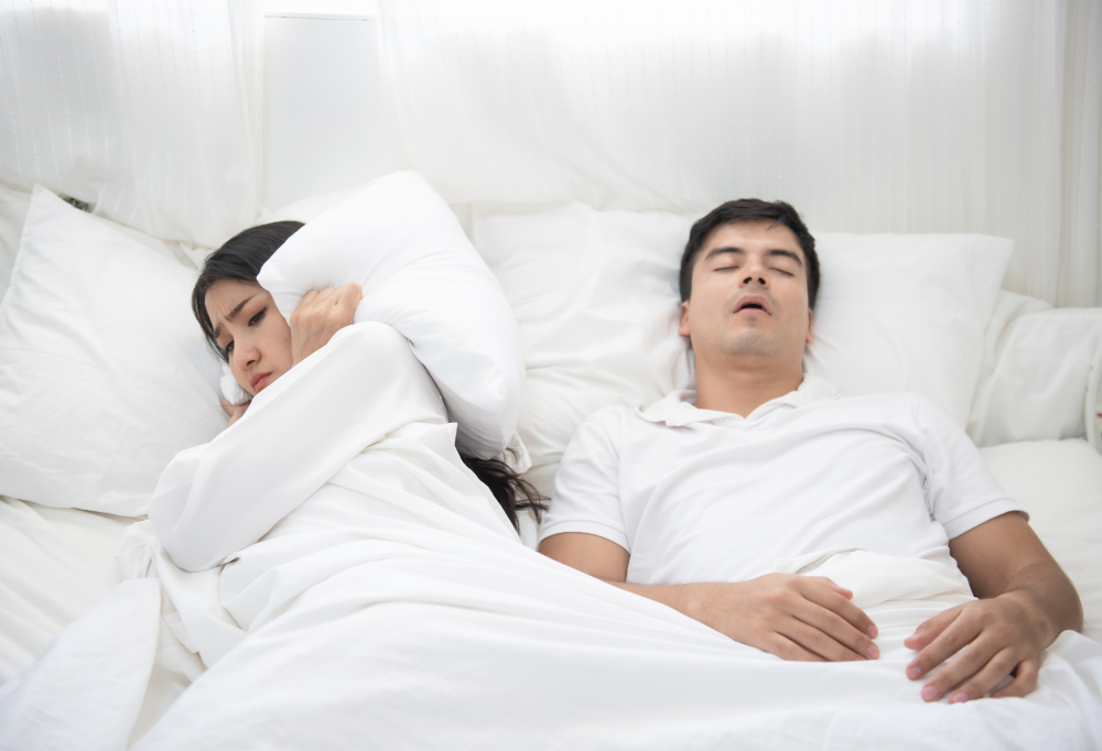女士因為身旁男士打鼻鼾而以手蓋著耳朵的圖片