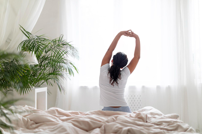 Image of a woman sitting on the bed and stretching her arms after waking up.